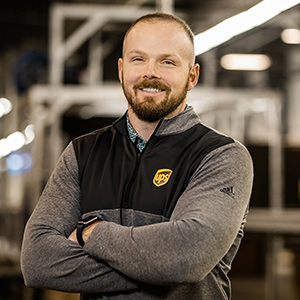 Smiling UPS employee wearing a UPS-branded sweater and standing in a facility