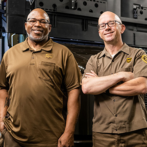 Zwei lächelnde UPS Circle of Honor Zusteller und Kollegen in derselben Einrichtung