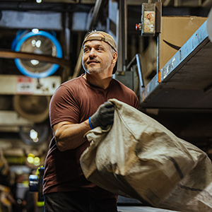 Part-time UPS employee in a warehouse lifting a packing bag.