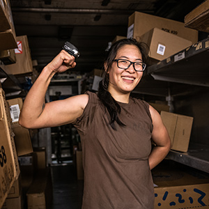 UPS Teilzeitmitarbeiterin steht in ihrem Paketwagen und lässt ihre Armmuskeln spielen.