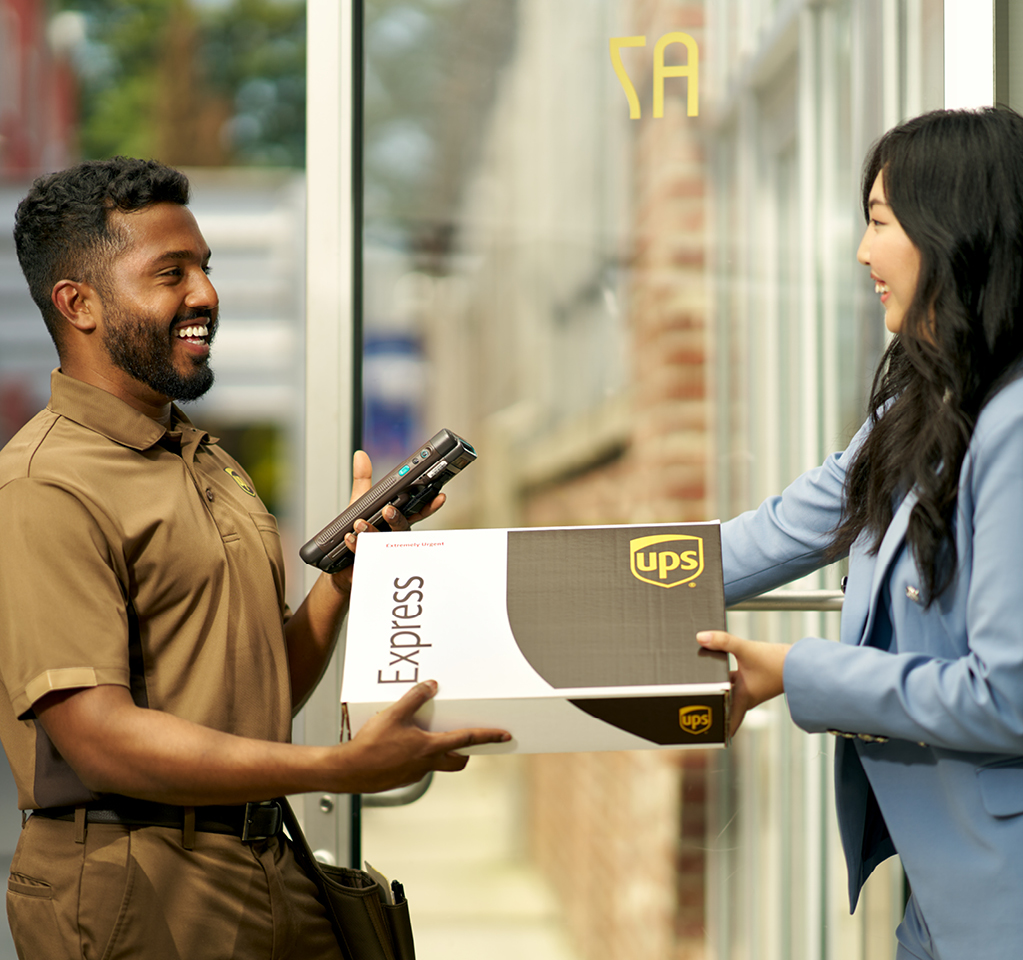 UPS delivery person hands a package to a woman in a blue blazer