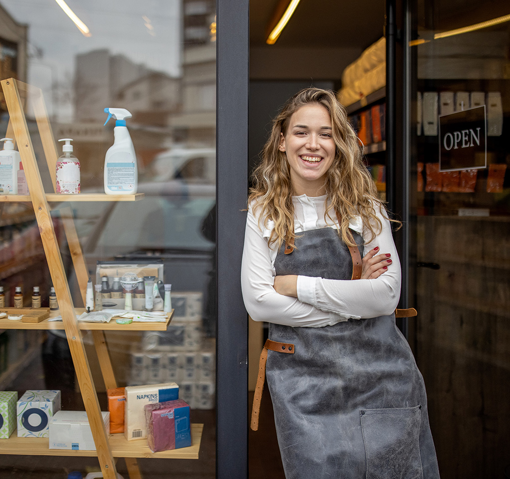 A small business owner stands outside the open door to her shop.