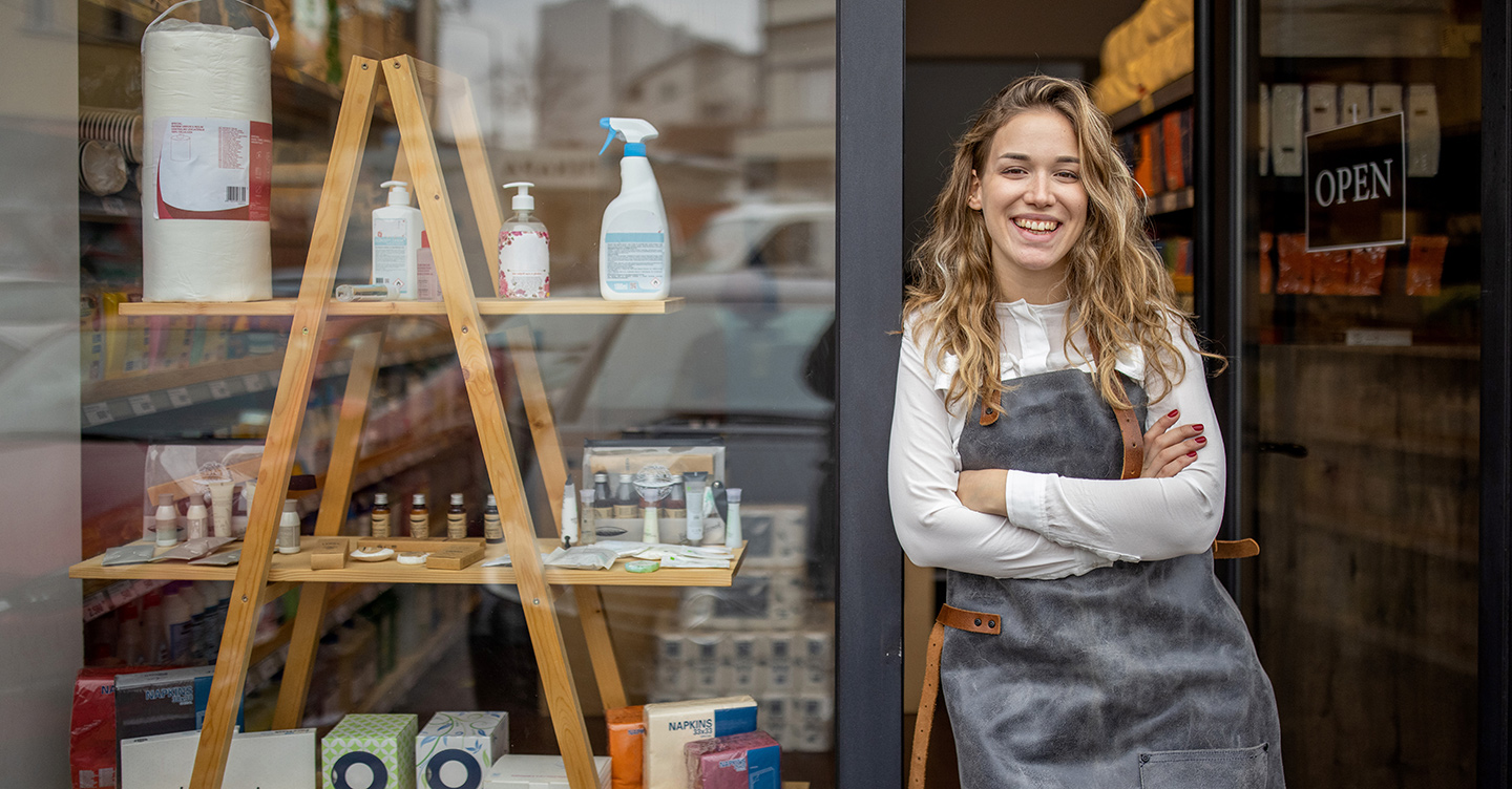 A small business owner stands outside the open door to her shop.