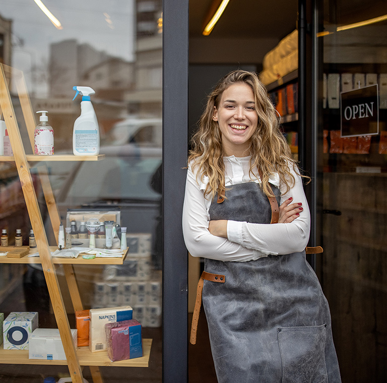 A small business owner stands outside the open door to her shop.