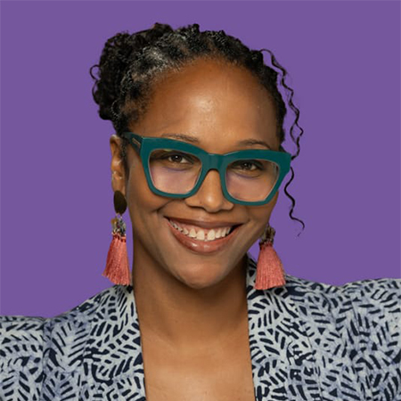 A portrait of Andrea C. Bibbs, smiling and wearing a patterned jacket in front of a purple background