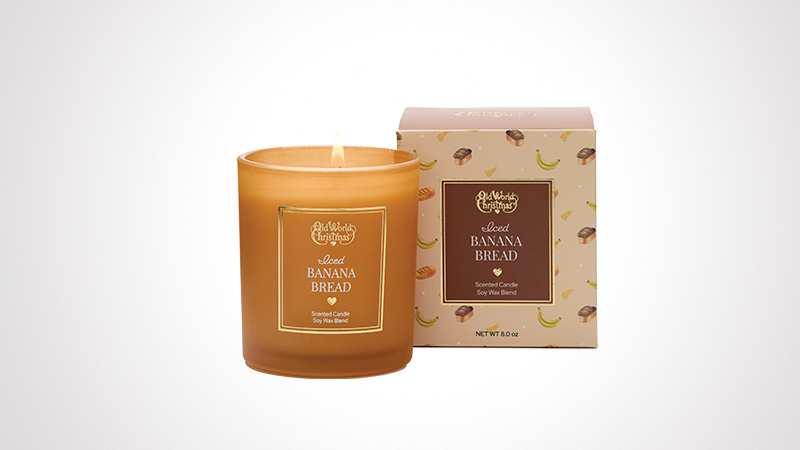 A warm-toned candle labeled 'Banana Bread' emits a cozy glow, paired with its decorative box featuring banana and bread illustrations. The packaging highlights the scent and includes the text 'Net Wt 8 oz'. Perfect for creating a comforting ambiance.