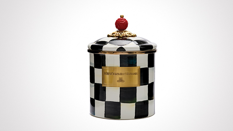 A decorative ceramic jar featuring a black-and-white checkered pattern and a gold plaque on the front. The lid is adorned with a red knob resembling a fruit and gold detailing. The jar has a luxurious and artistic design, suitable for home decor or storage.