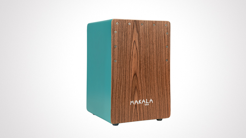 A Makala cajon featuring a wooden front panel with a natural grain texture and teal-colored sides. The cajon is designed for percussion performances and has visible screws on the front panel for structural integrity. The Makala logo is clearly displayed on the wooden surface.