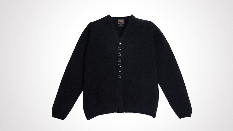 A classic black cardigan featuring a V-neck design and button-up closure. The garment is displayed against a clean white background, emphasizing its simple and timeless style. The texture and detailing of the fabric are clearly visible, making it suitable for casual or formal settings.